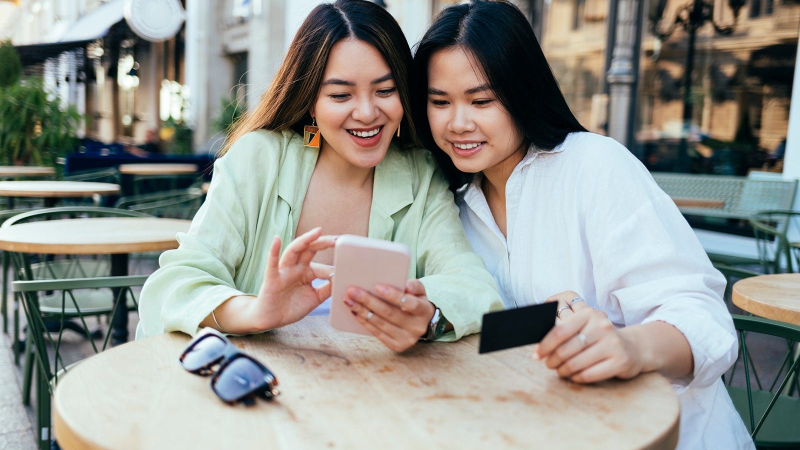 Smiling women shopping online through smart phone at sidewalk cafe