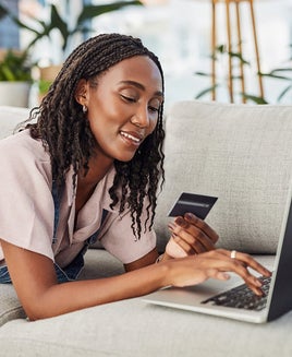 Online shopping, woman with laptop and credit card for payment on a sofa in living room of her home. Ecommerce, investment or pay bills and African female person with bank information for internet