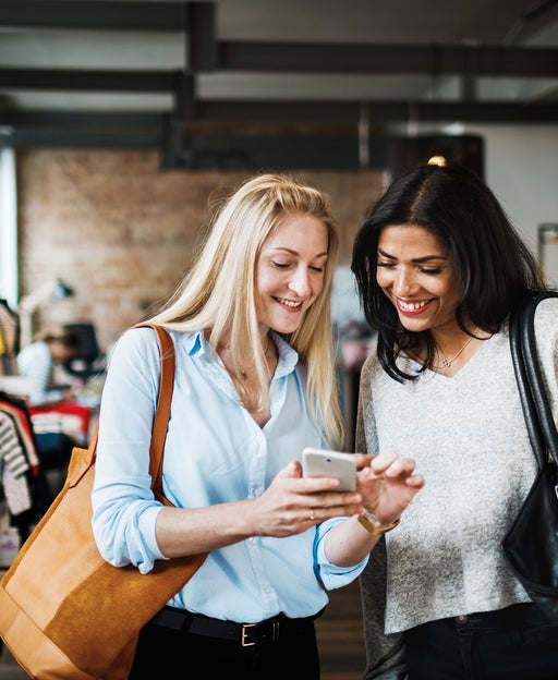 Two Womem Looking At Smartphone While Clothes Shopping