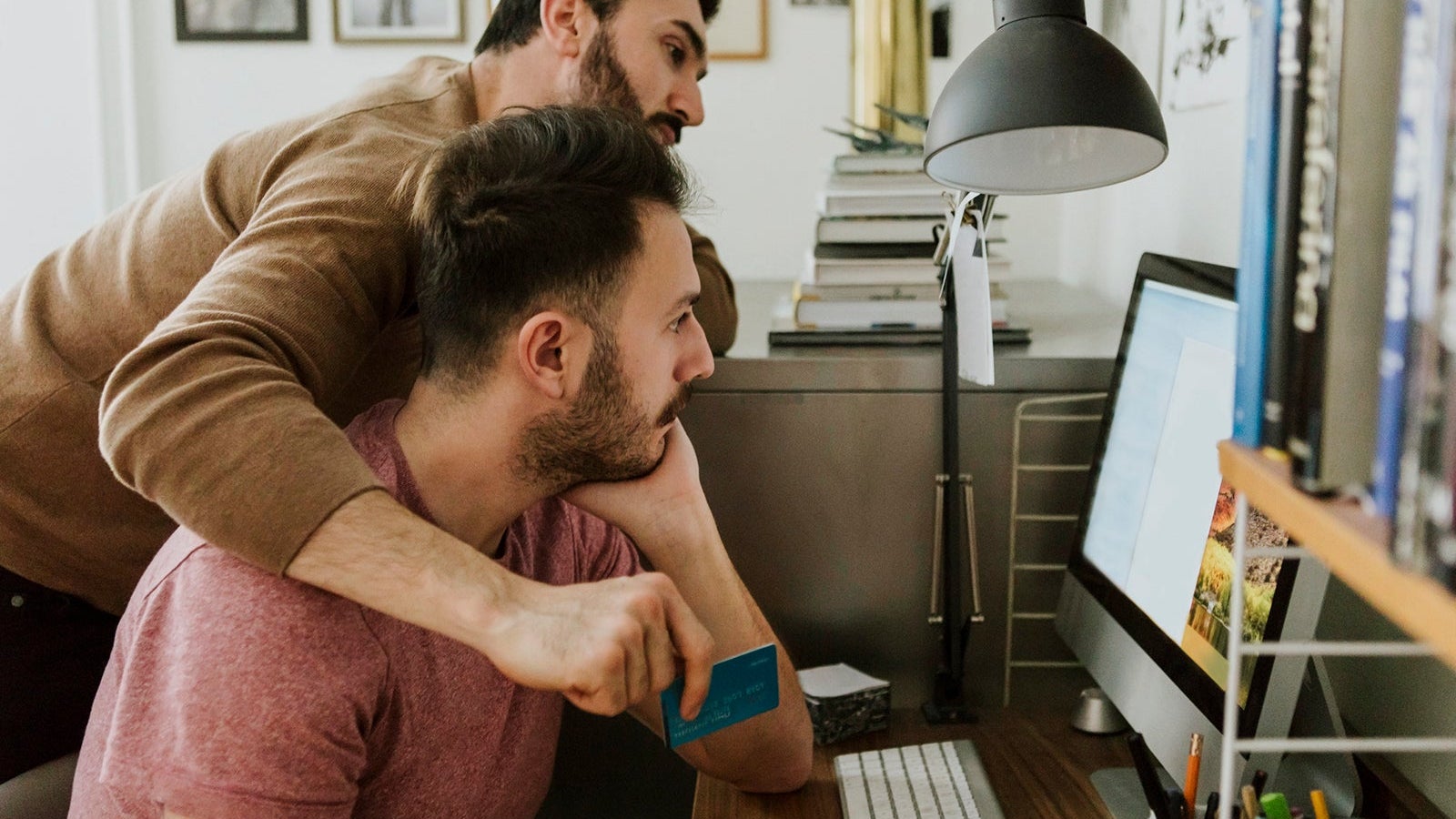 Gay couple shopping online through credit card on computer at home