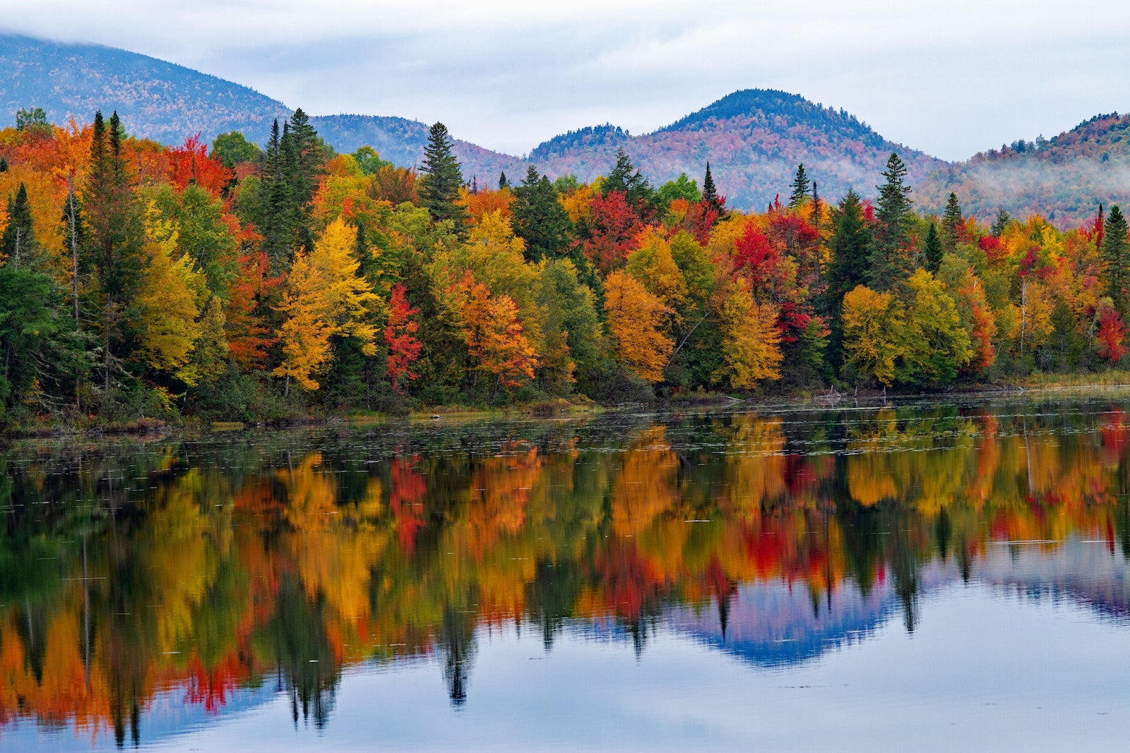 Here's where you can see fall foliage across the US in 2025 red, yellow, orange and green trees reflected in a lake