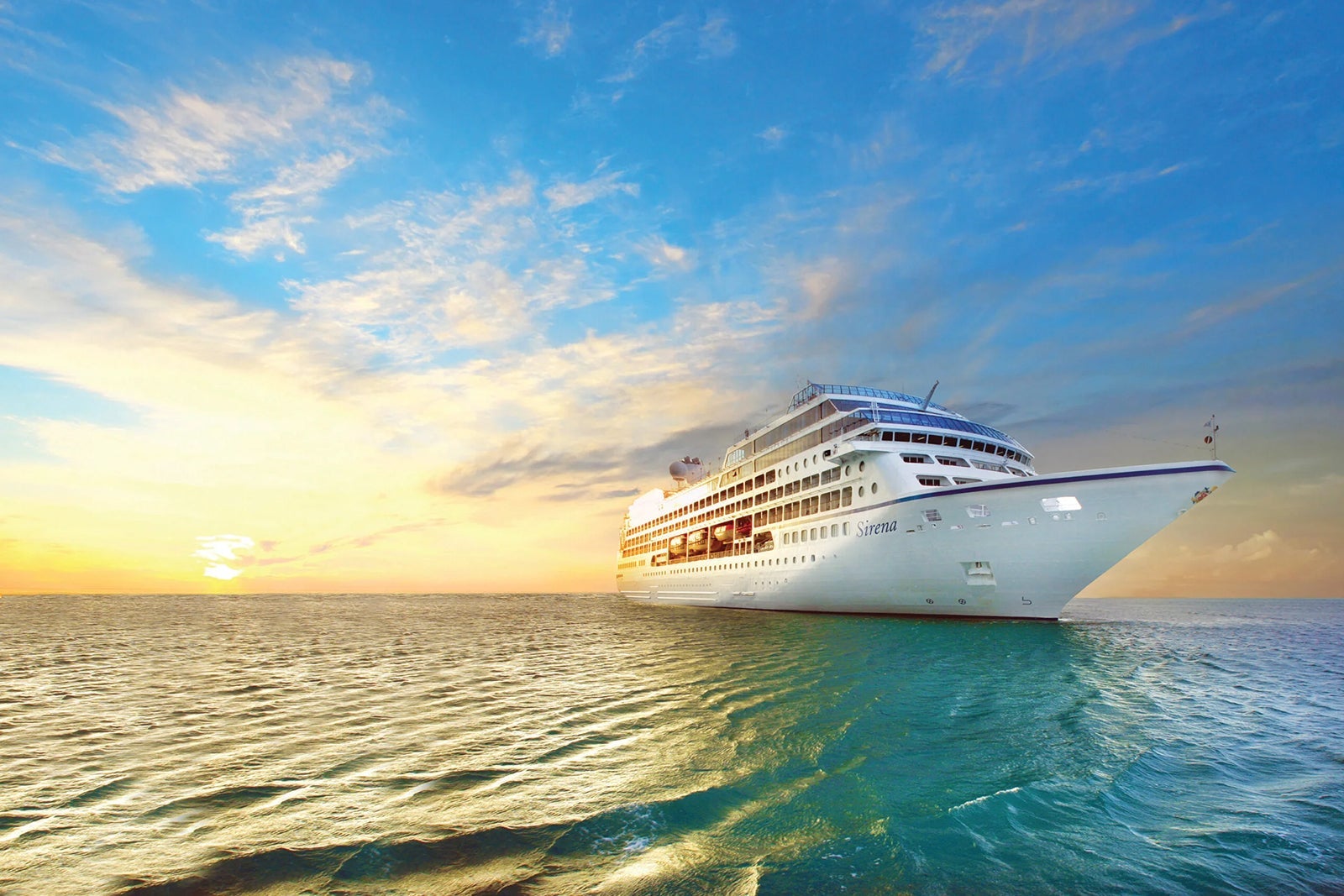 A cruise ship floats atop teal water just before sunset with blue sky and clouds in the background