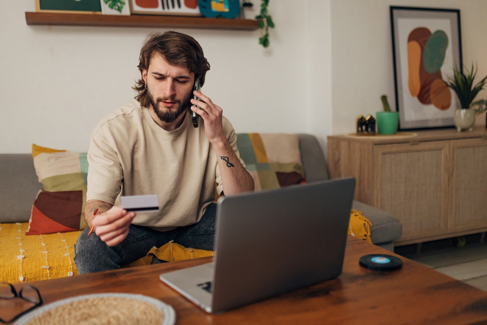 A young man holding a credit card while on the phone, looking perplexed