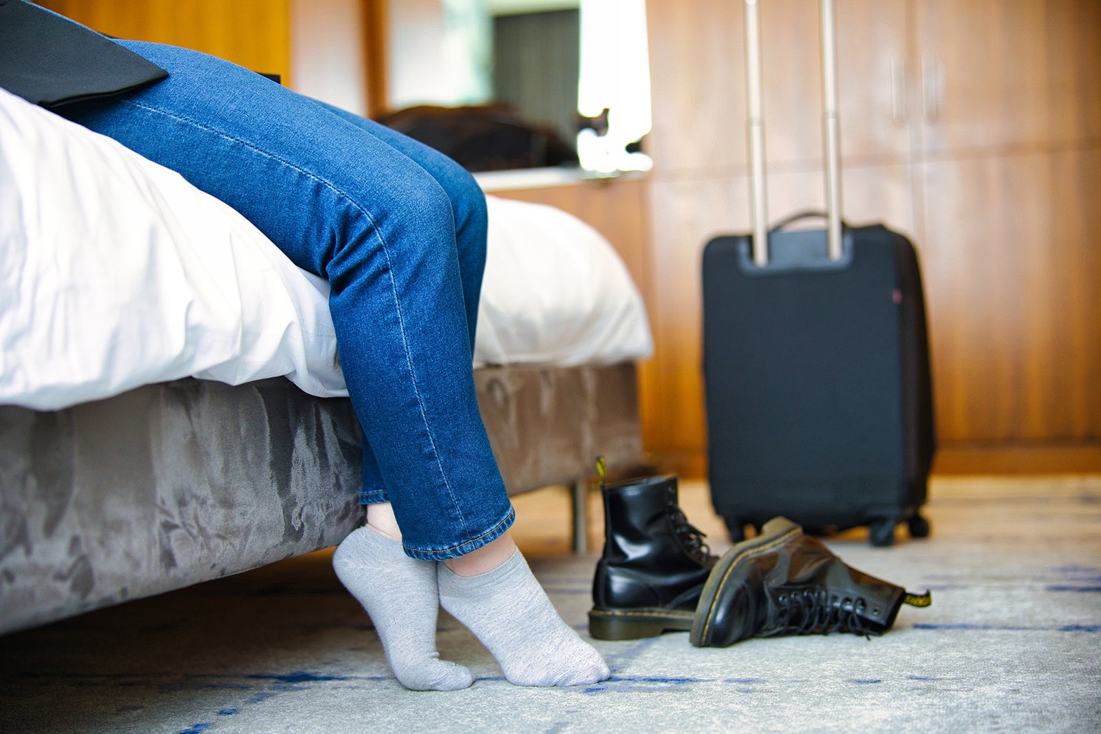 A traveler taking off their shoes while sitting on a bed