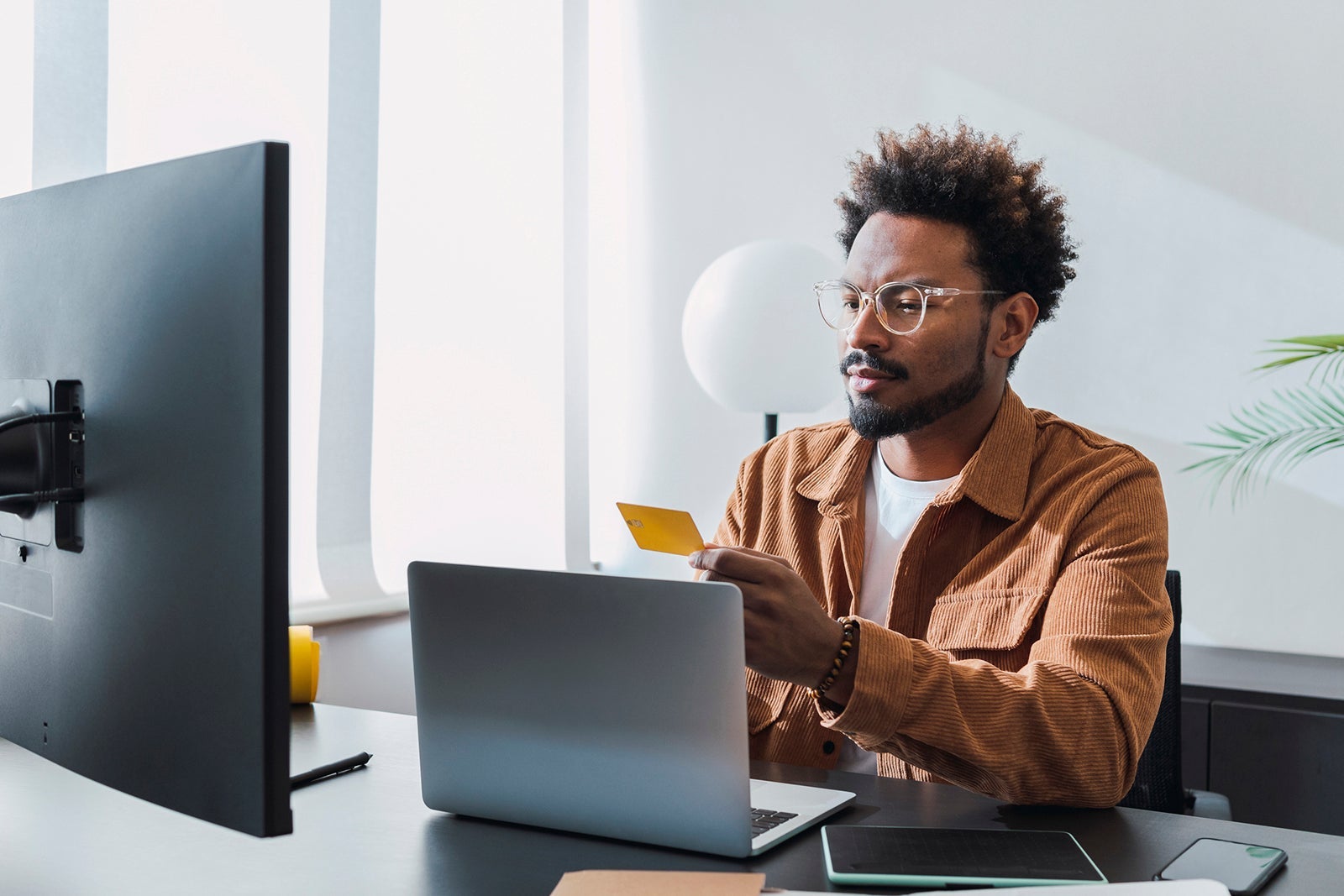 Man looking at a laptop and monitor holding a credit card