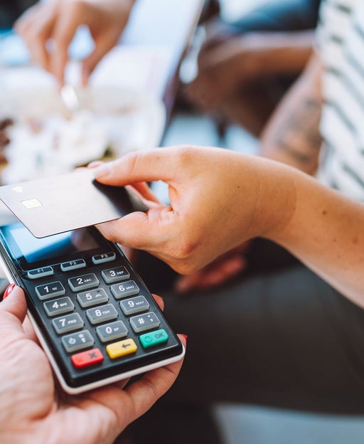 Tap to pay, cashless. Cropped woman hand holding credit card to pay in cafe for food and drinks. Focus on hand and card reader. Close up