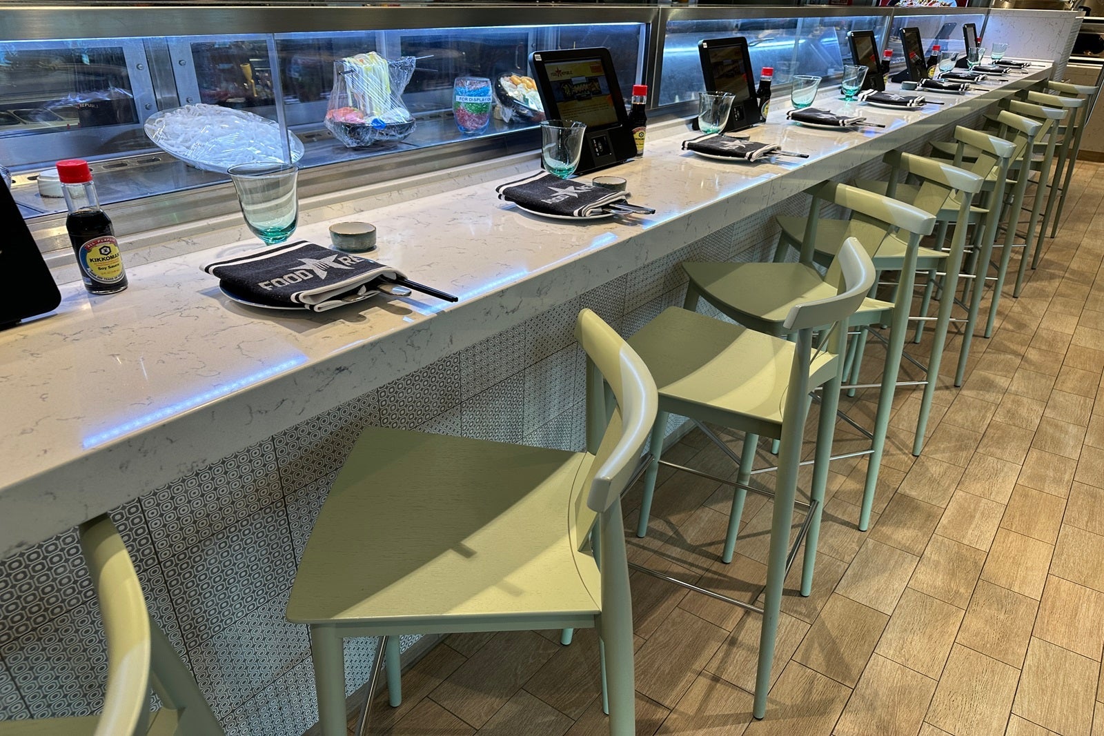 A sushi bar with green high-top chairs turned on an angle and place settings
