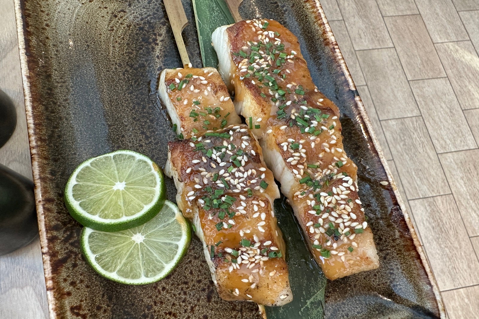 Pieces of blackened fish on wooden skewers on a plate garnished with limes