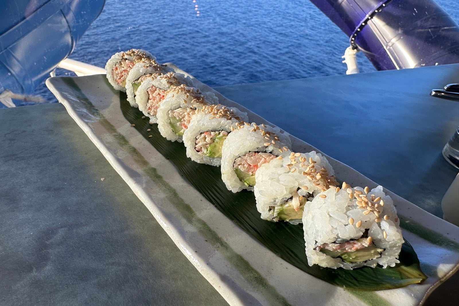A sushi roll on a long plate in front of a window on a cruise ship