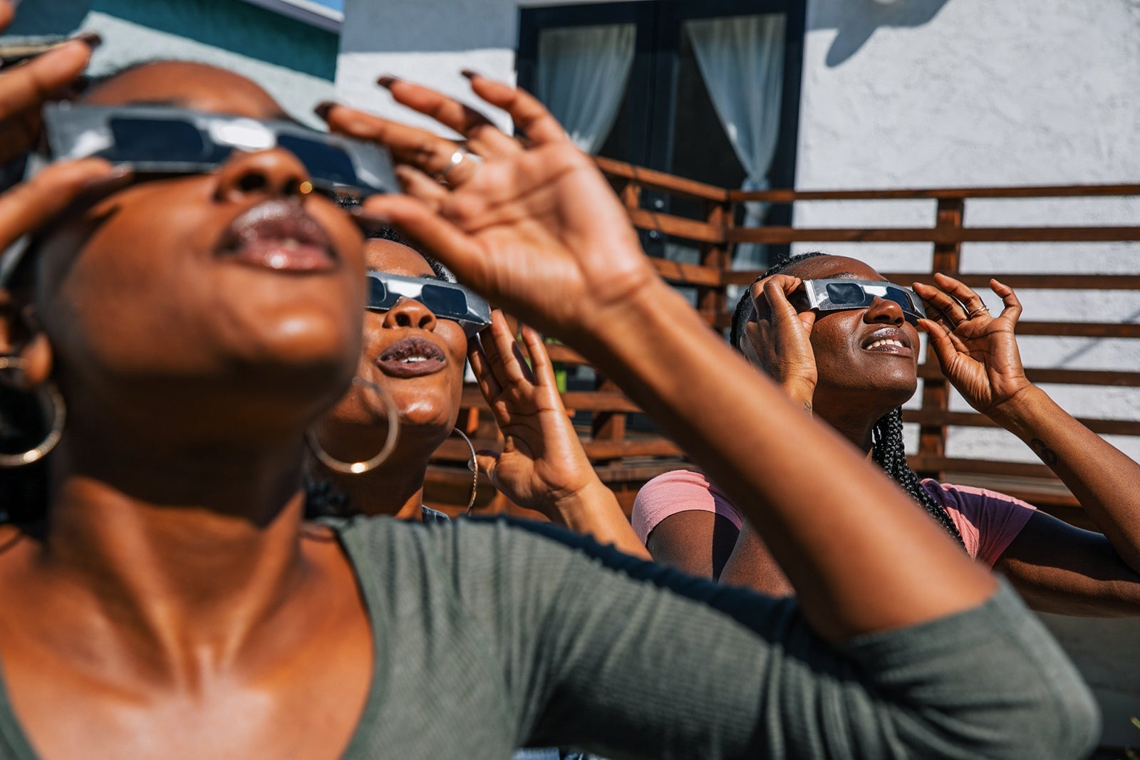 Women friends at home enjoying solar eclipse looking at the sun with eclipse sunglasses. LEOPATRIZI/GETTY IMAGES