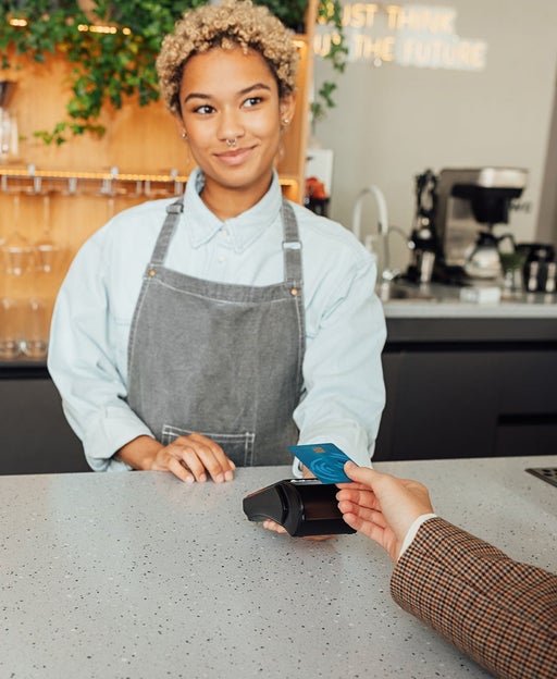 Woman bartender receives payment from a customer. Barista in apron holding pos terminal while customer paying buy card.
