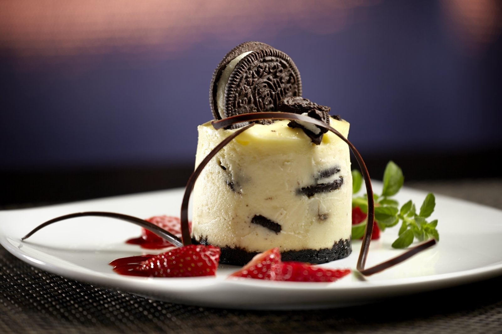 A cylindrical cookies and cream cheesecake dessert with strawberries on a plate
