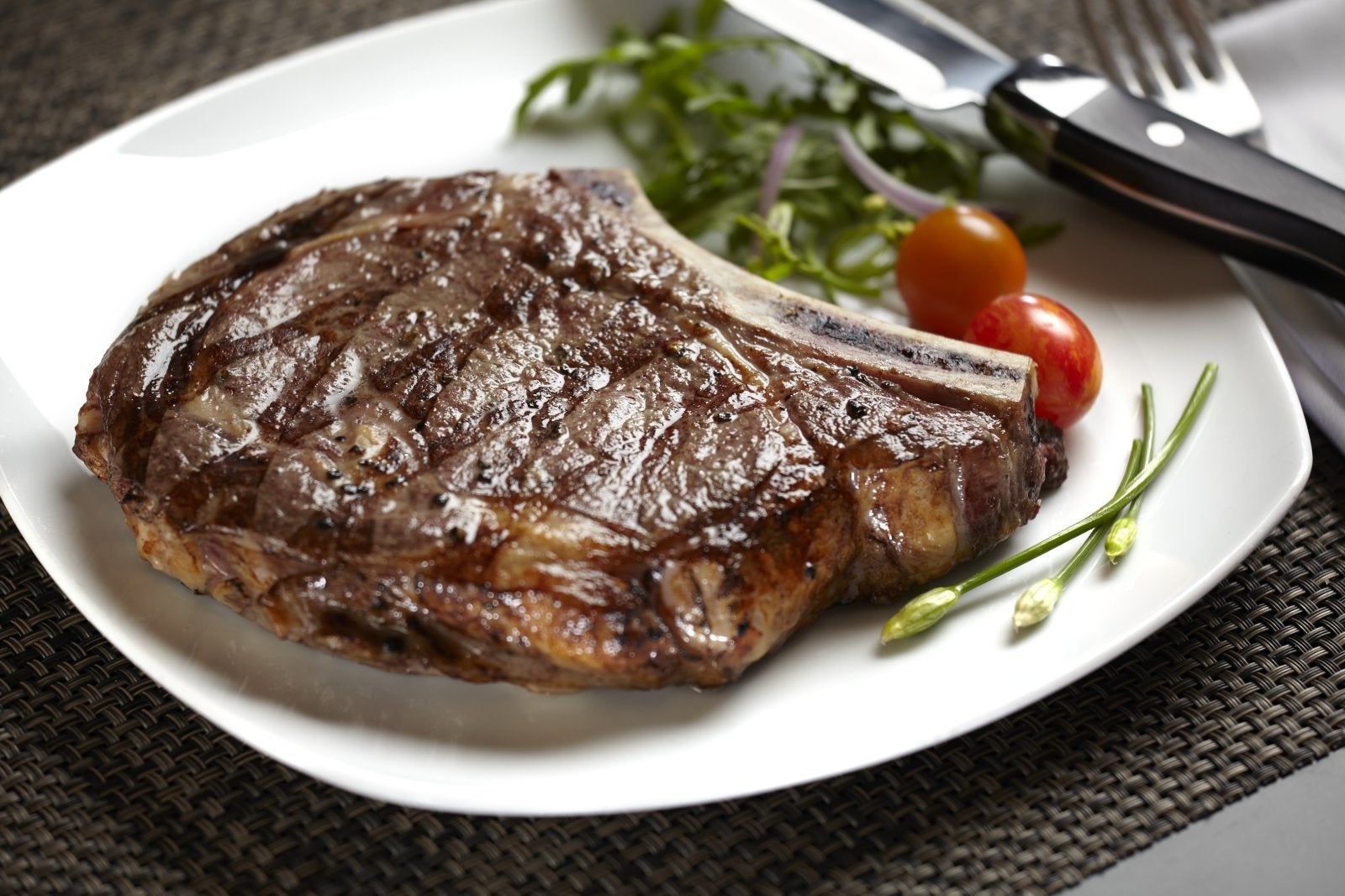 A plate with a steak, greens and tomatoes