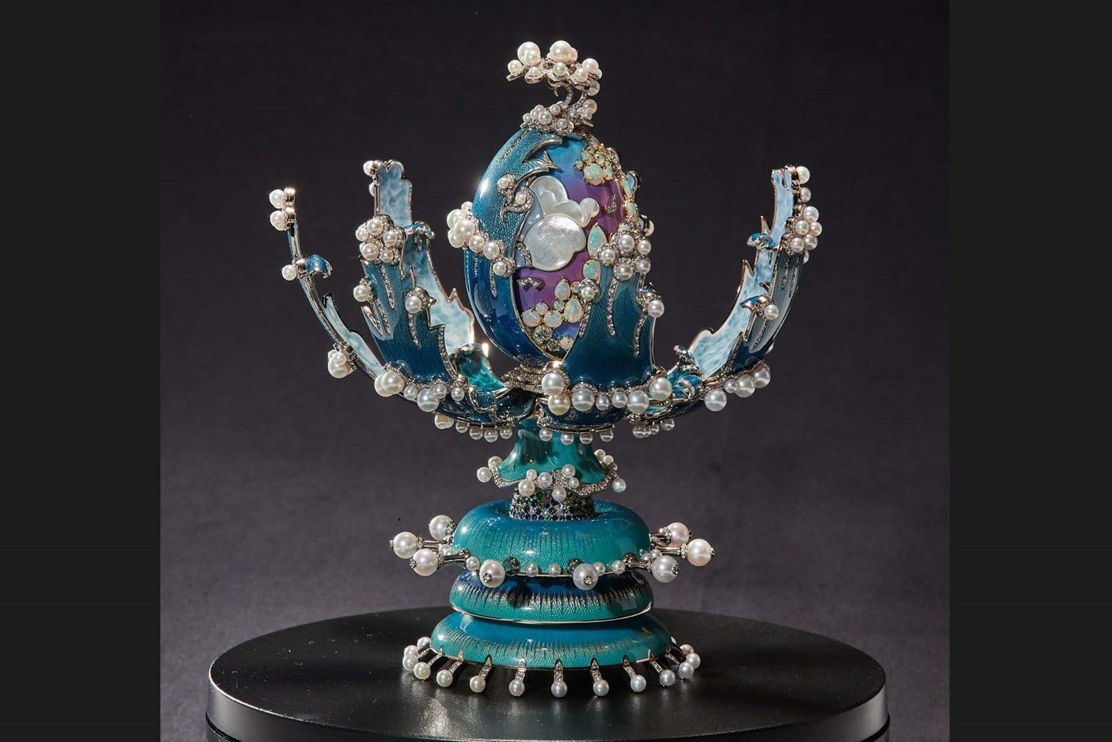 An ornate, bejeweled sculpture of a teal egg that has opened to reveal a second egg inside