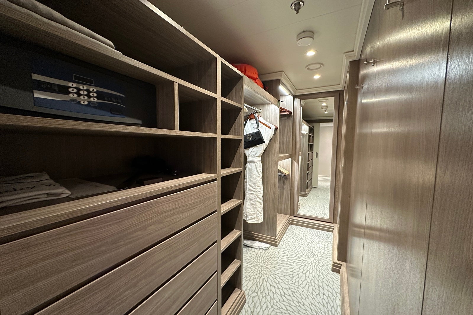 The inside of a walk-in closet in a cruise ship cabin with shelves, drawers and a robe hanging on a bar