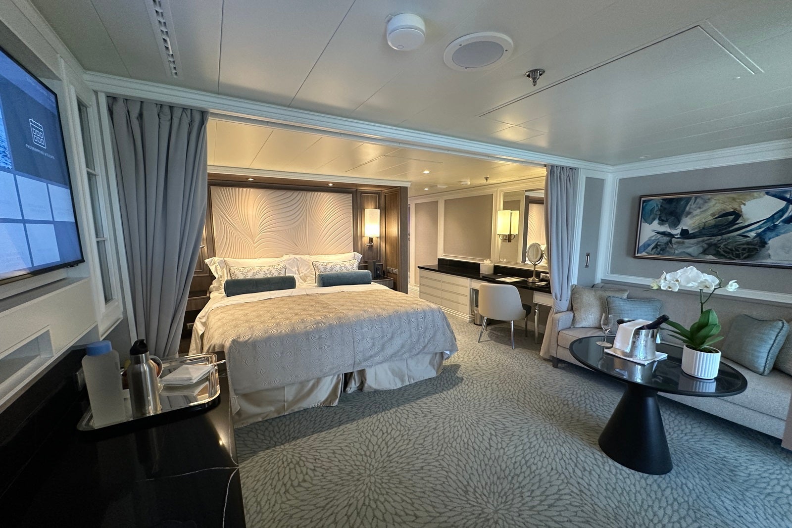 A cruise ship cabin showing a queen bed, vanity and sofa with a coffee table