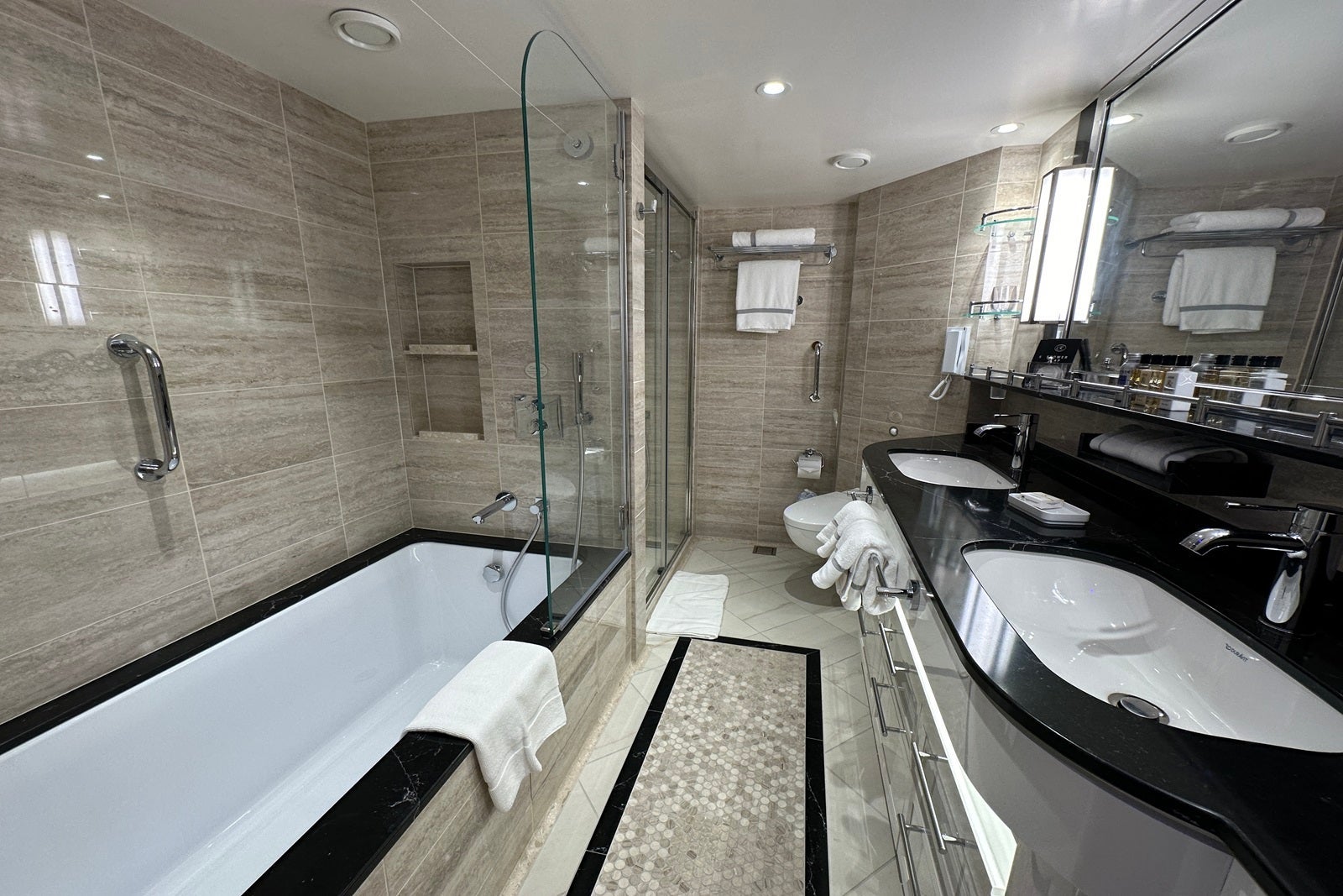 A marble cruise ship bathroom with a dual-sink vanity, a bathtub, a shower and a toilet