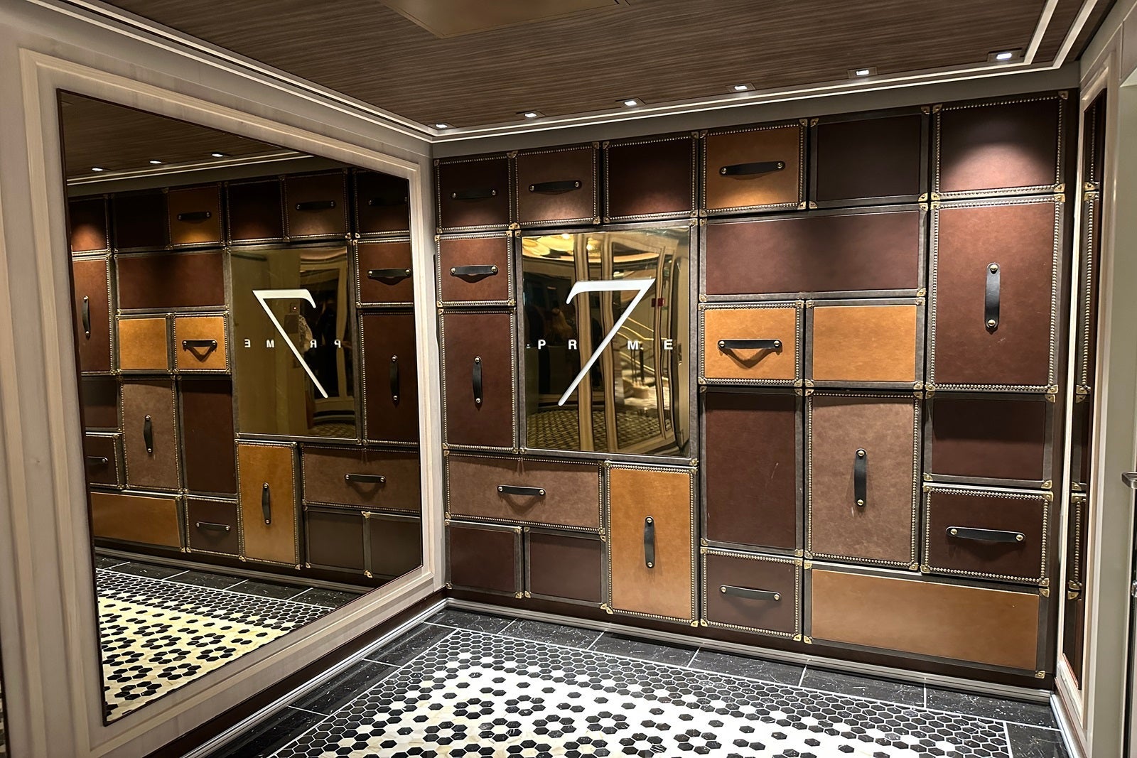 A wall adorned with brown leather rectangles with handles that look like suitcases with a black-and-white mosaic floor in front