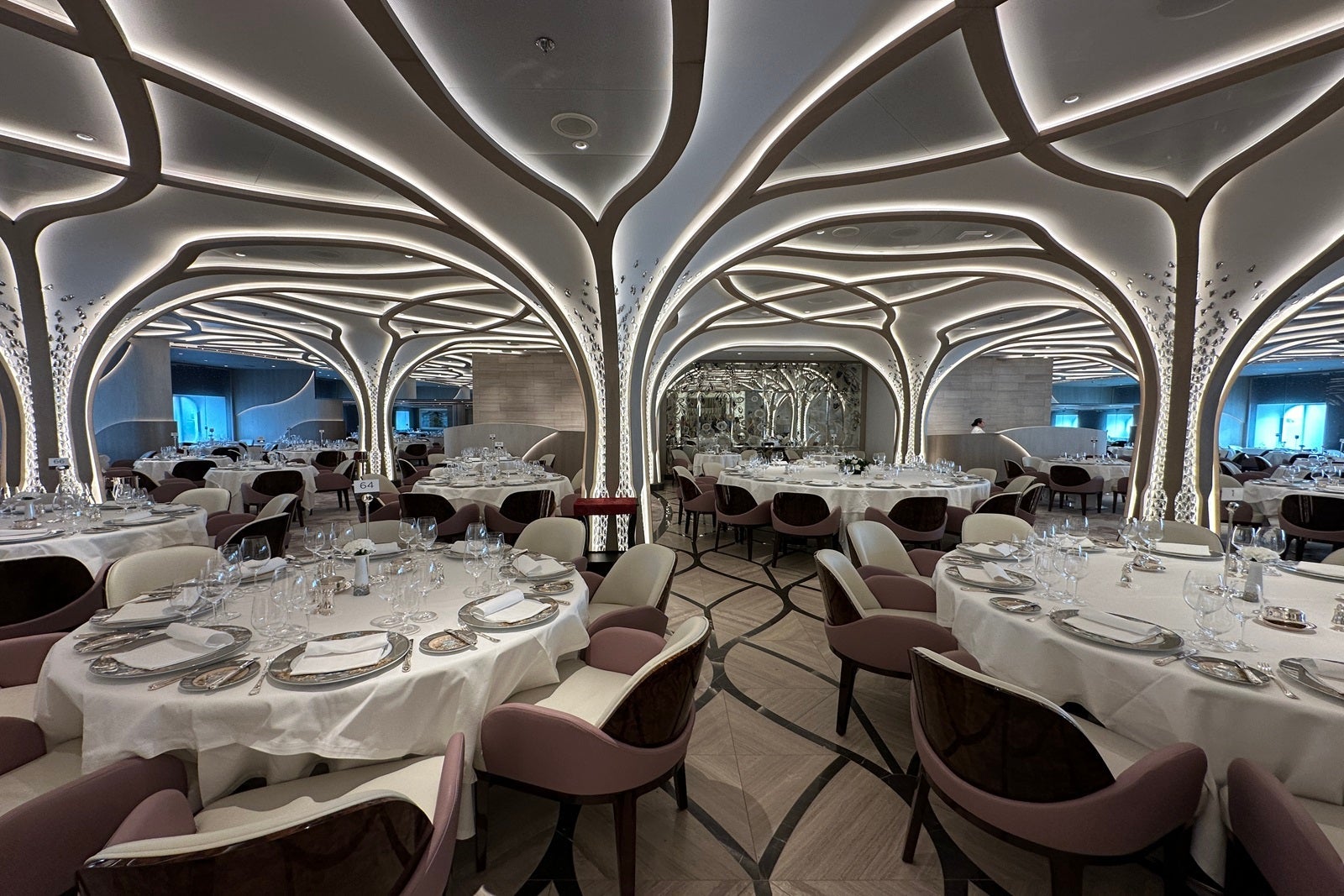 A large dining room with set dinner tables and artistic lights that rise from floor to ceiling along columns