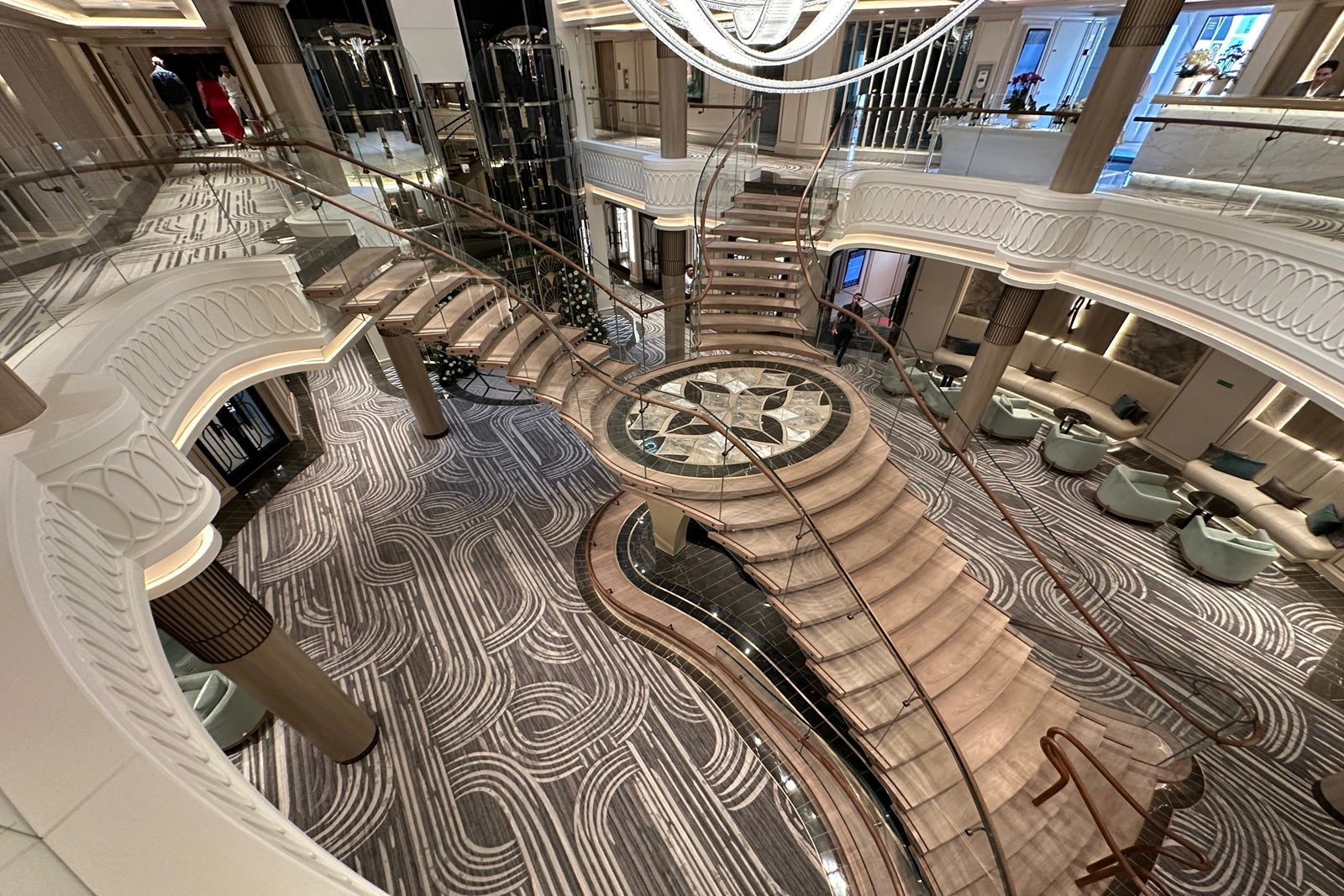 A split staircase rises two decks in the atrium of a cruise ship while glittering lights shine overhead
