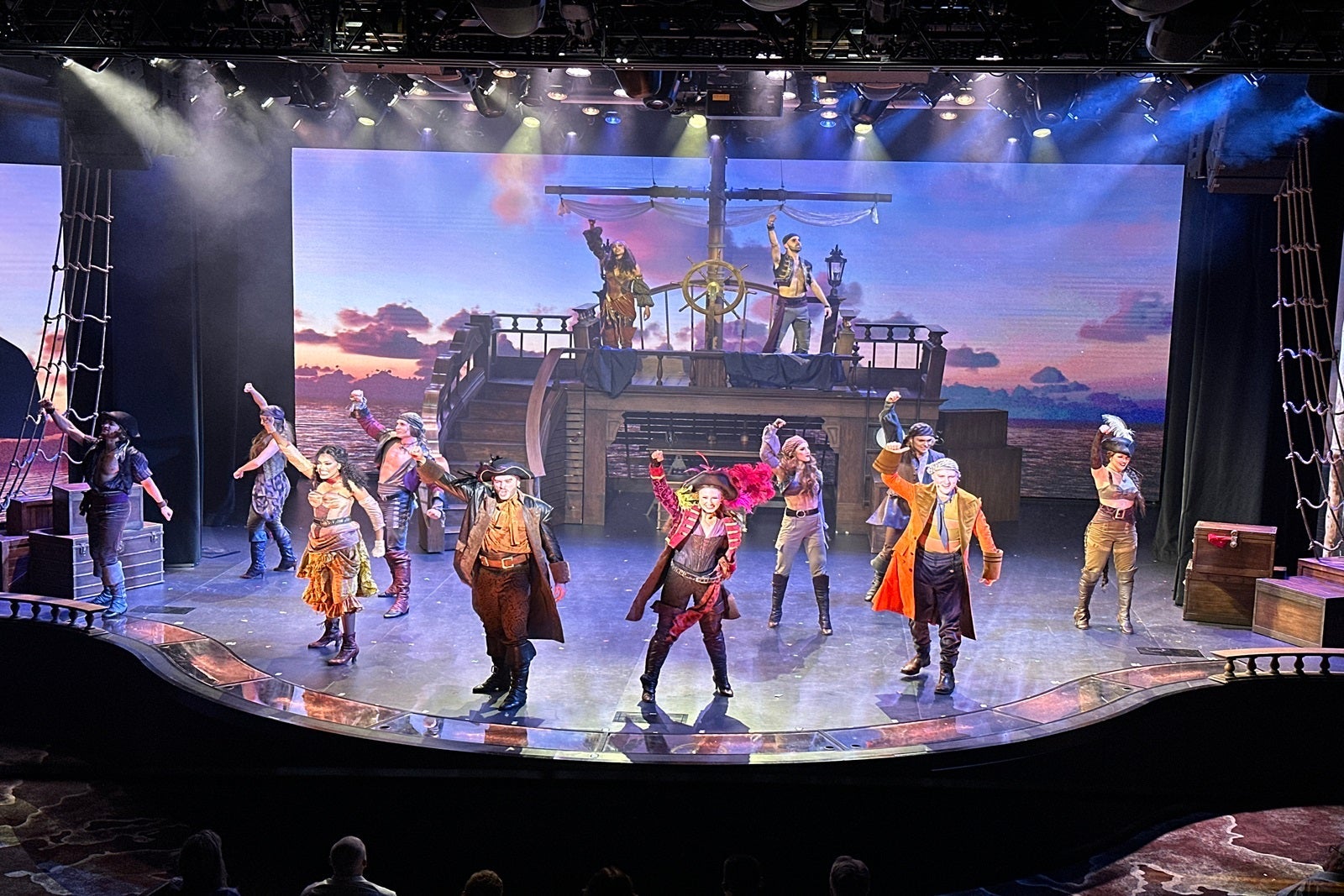 Performers dressed as pirates stand on a stage set up like a pirate ship and throw their fists in the air