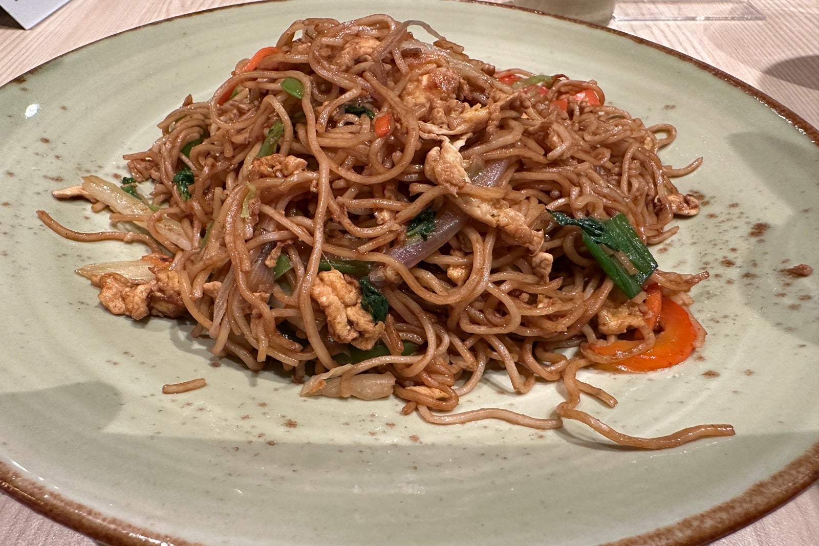 A plate of thin Asian noodles prepared with vegetables on a white plate