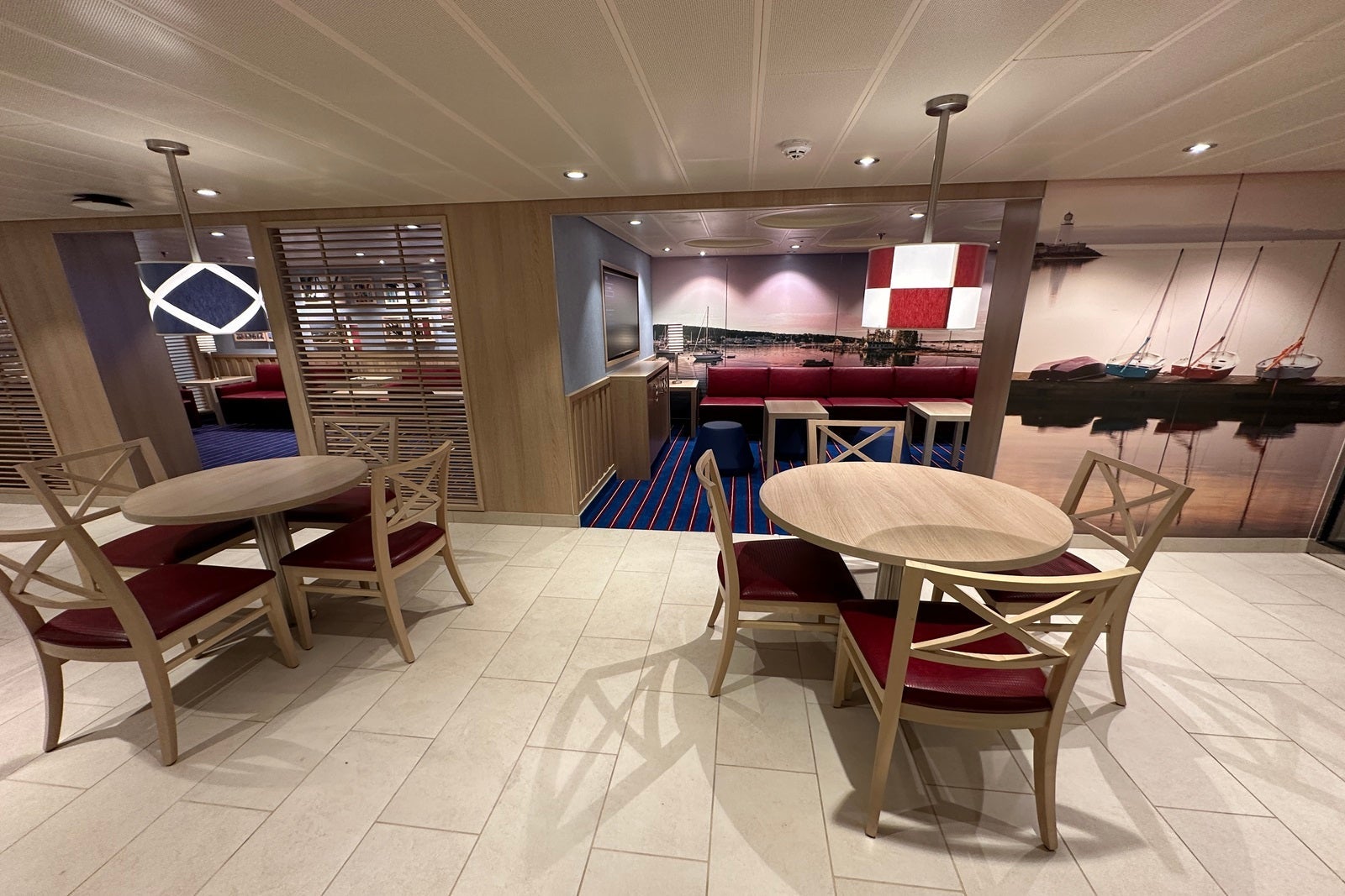 A nautically themed lounge area with light woods, tables with chairs, and red and blue decor