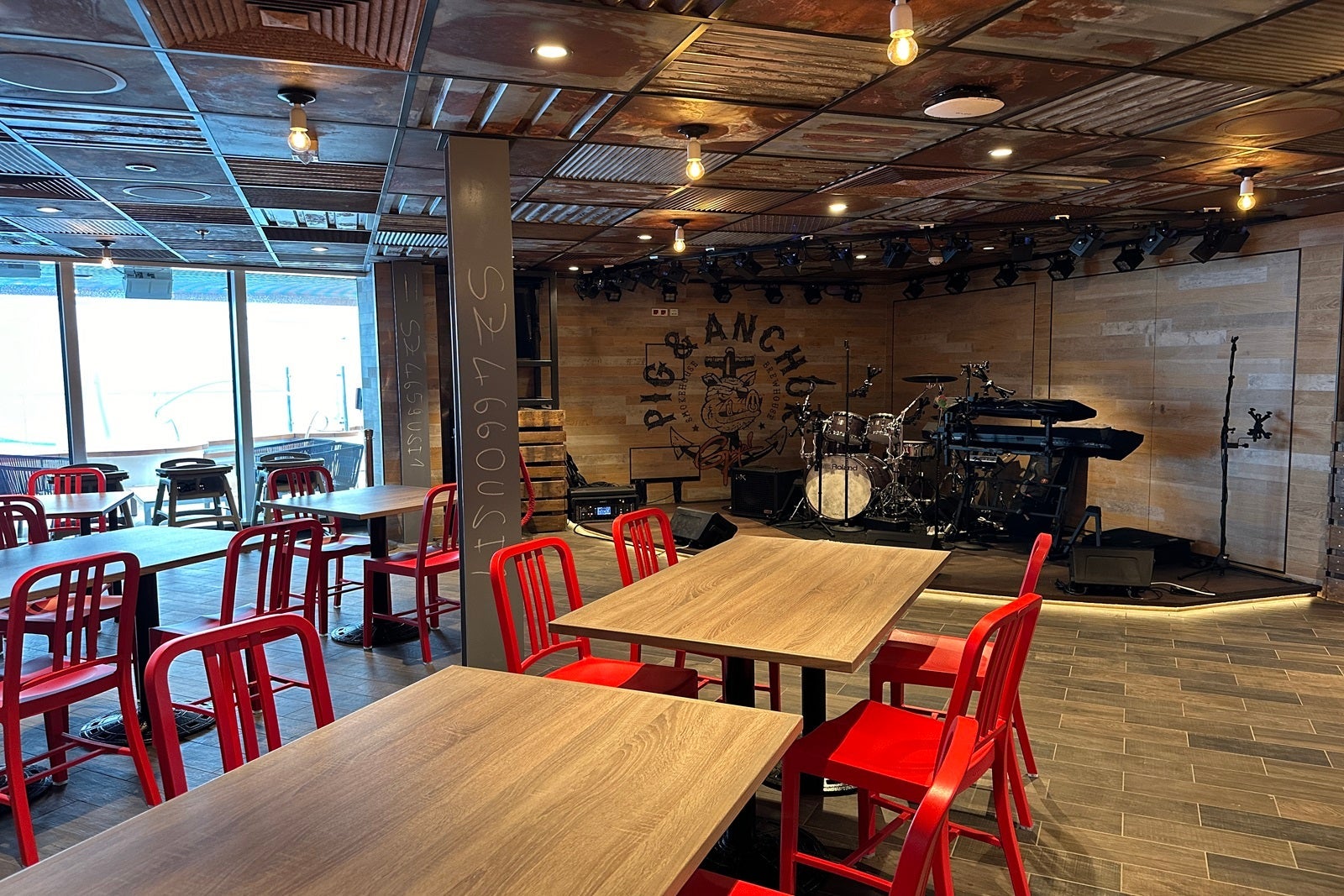 Wooden tables with red metal chairs near a small live-music stage