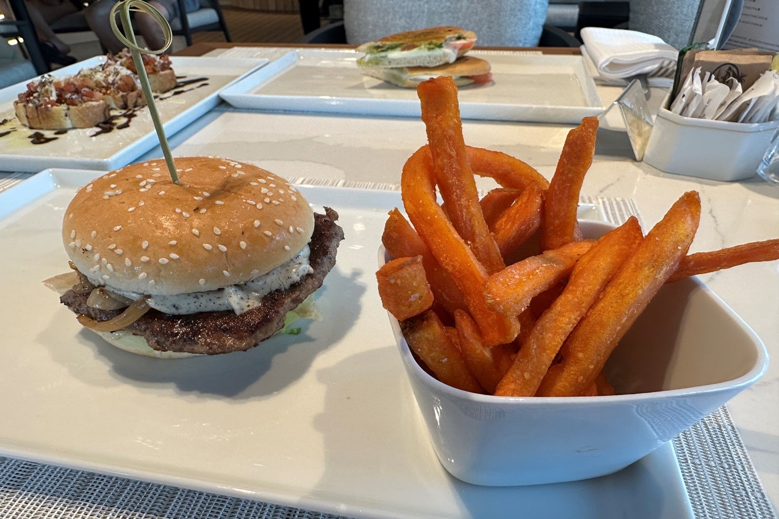 A cheeseburger sits on a plate next to a small bowl of sweet potato fries