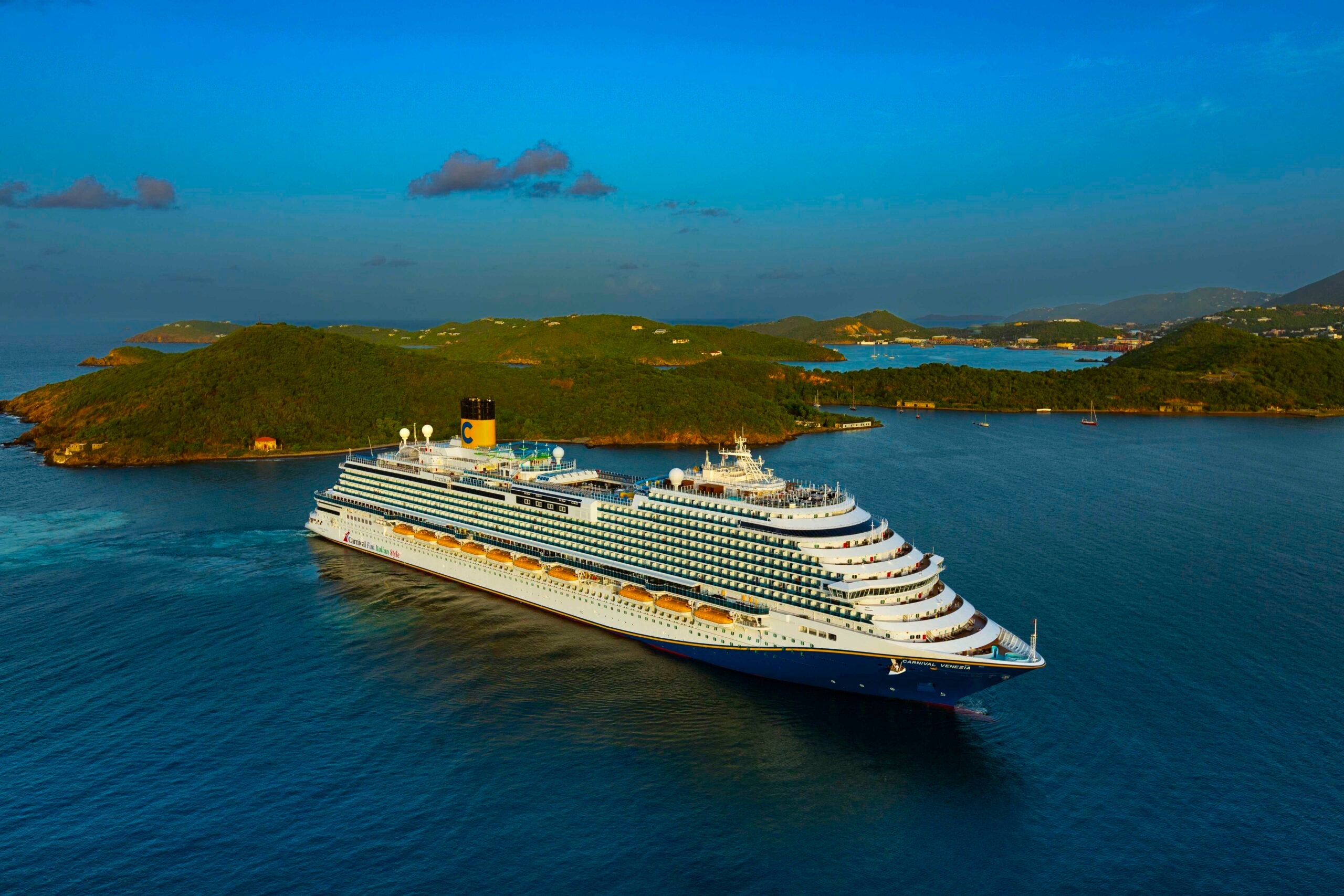 Carnival Venezia cruise ship anchored on teal water with islands and blue sky in the background