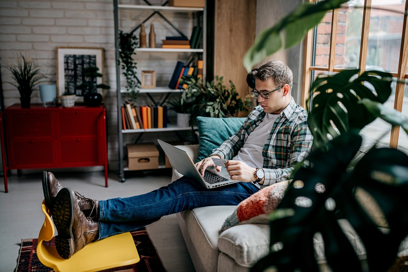 man sitting on a couch using a laptop while holding a credit card
