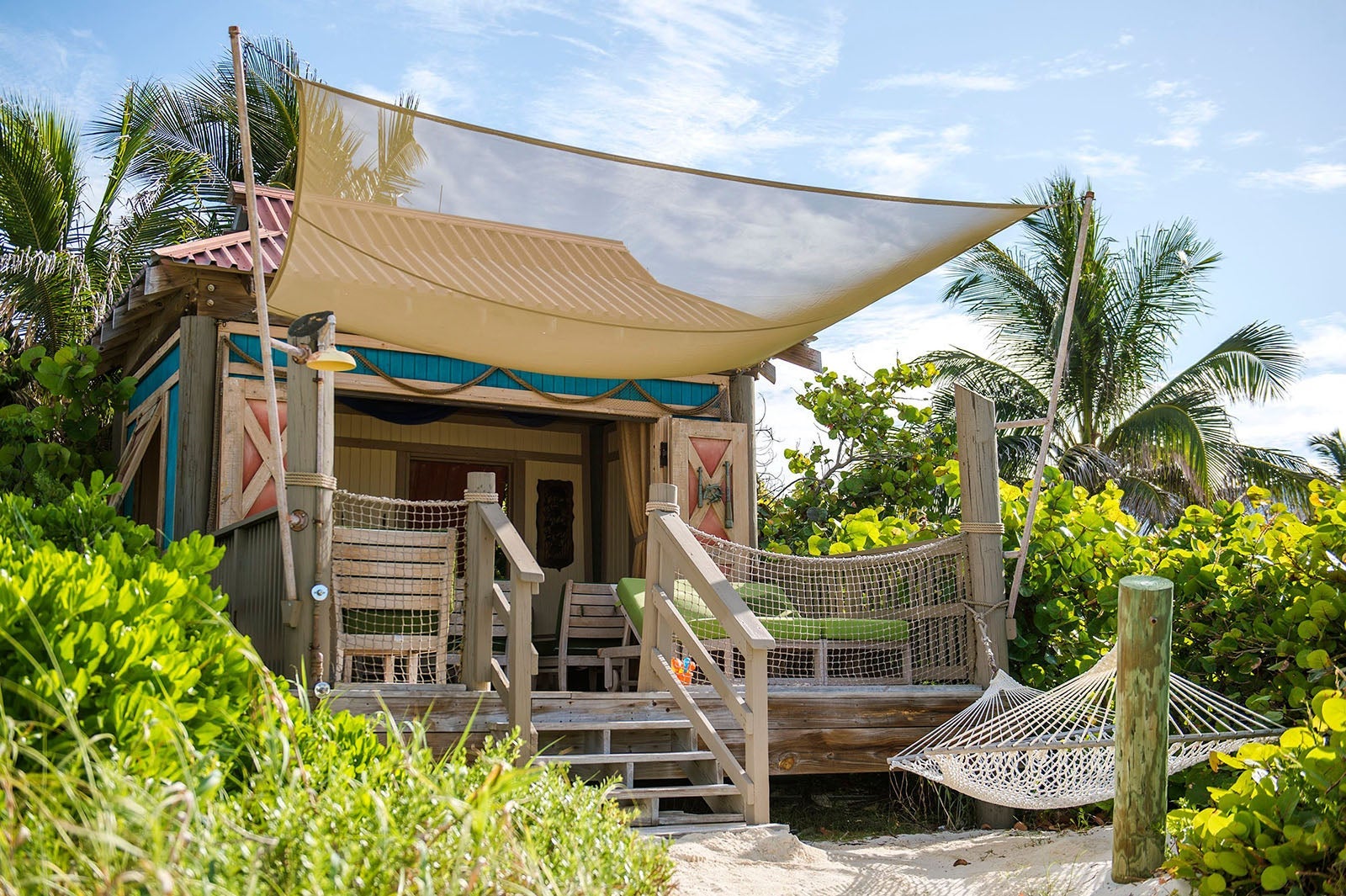 Wooden cabana with deck, padded lounge chairs and hammock in front on tropical island