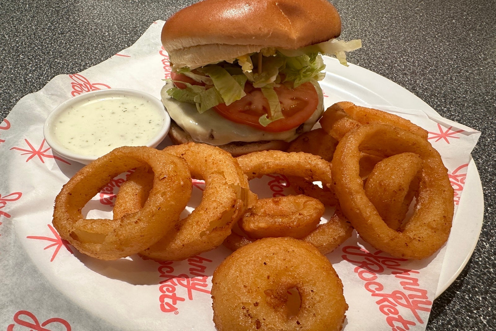 A cheeseburger with onion rings and a side of dipping sauce