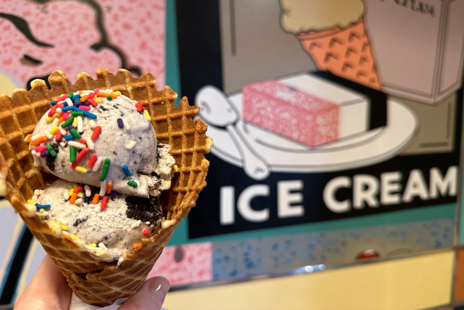 A cone of ice cream with sprinkles in front of a sign that says "ice cream"
