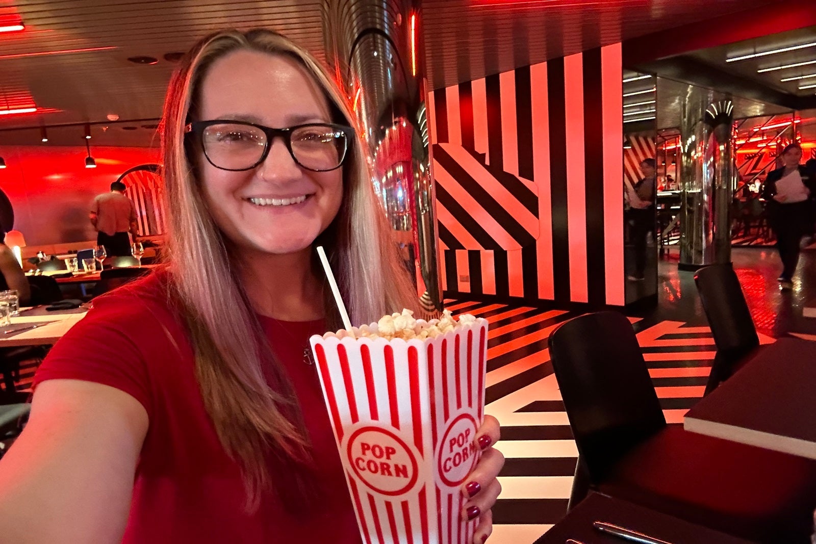 A woman in a red shirt holding a drink that looks like a bag of popcorn