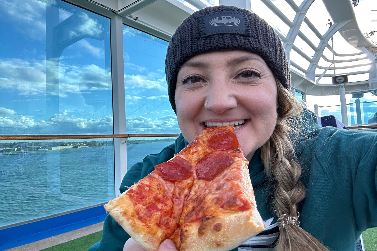 A woman in a black hat eating a slice of pepperoni pizza