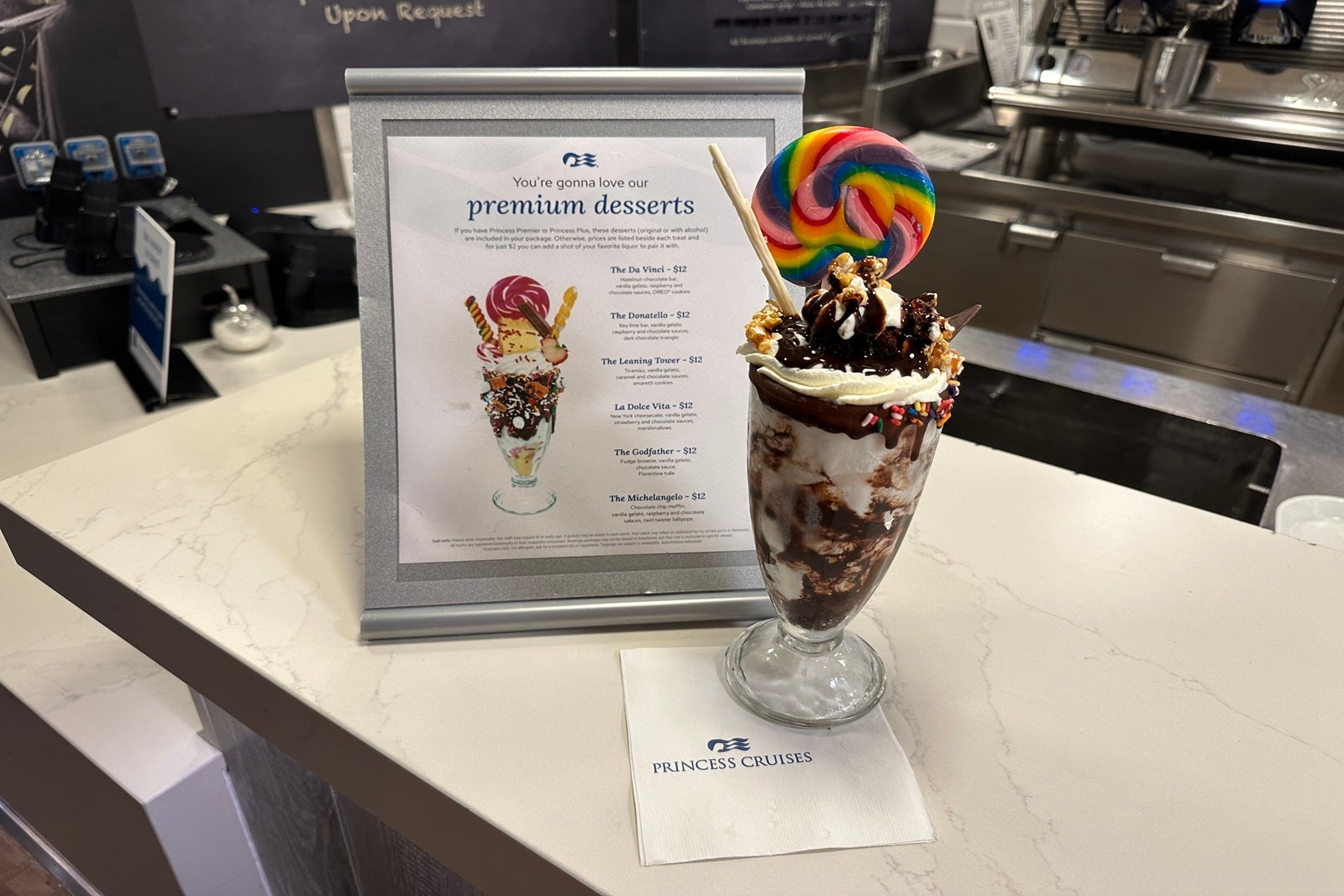 A large ice cream sundae topped with candy and a lollipop on top of a napkin in front of a sundae menu