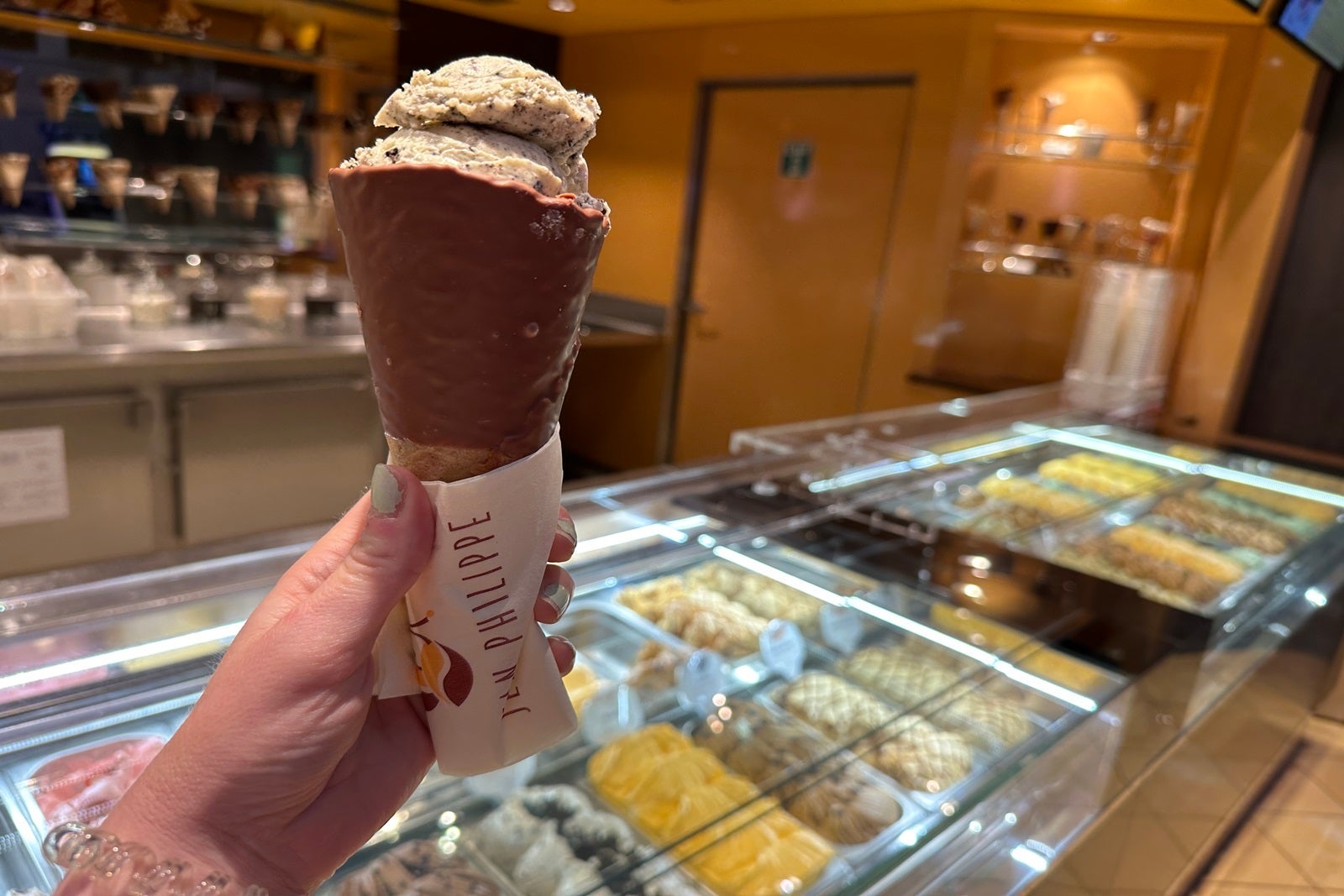 A hand holding a cone of gelato in front of a gelato display case