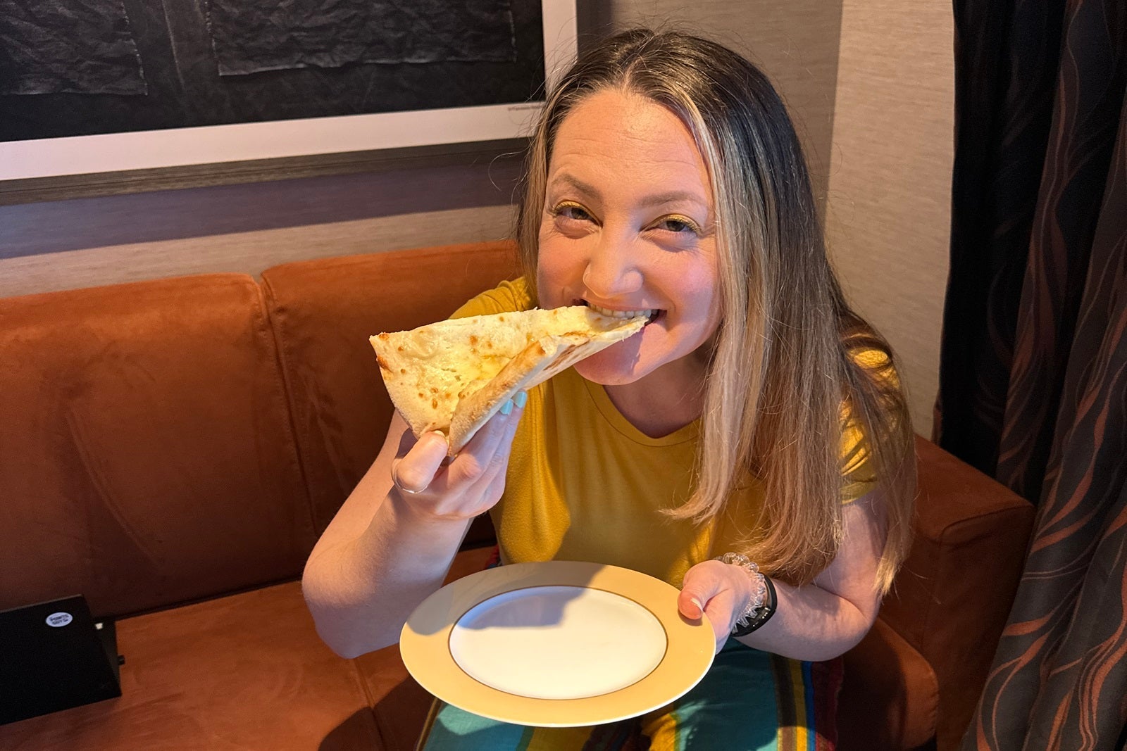 A woman sitting on a sofa eating a slice of pizza