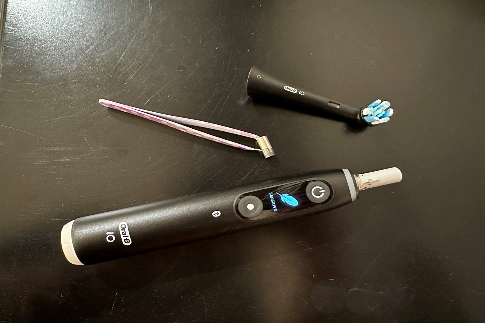 An electric toothbrush handle and brush head sit on top of a black counter with tweezers
