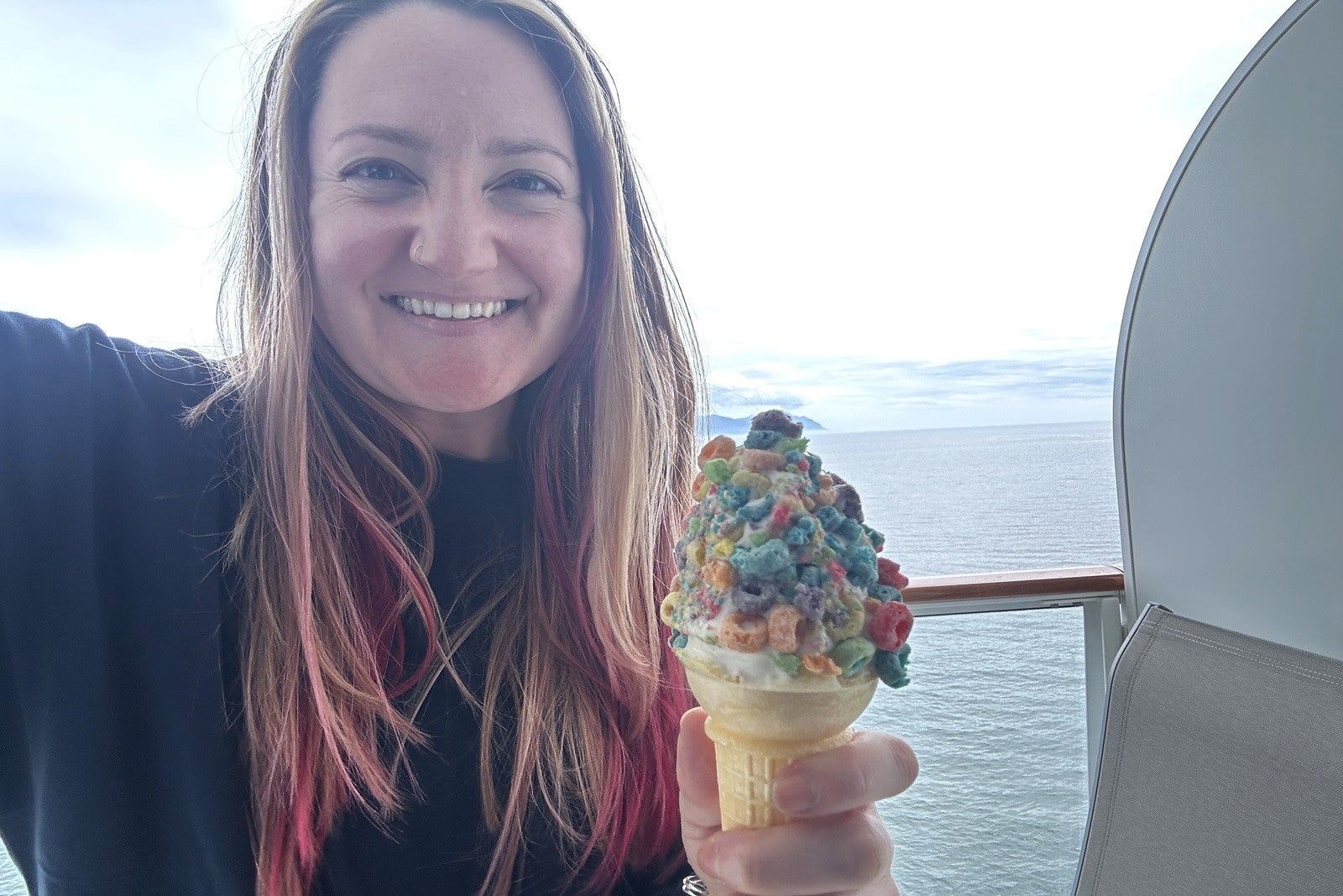 A woman holding a cone of soft-serve ice cream topped with Froot Loops