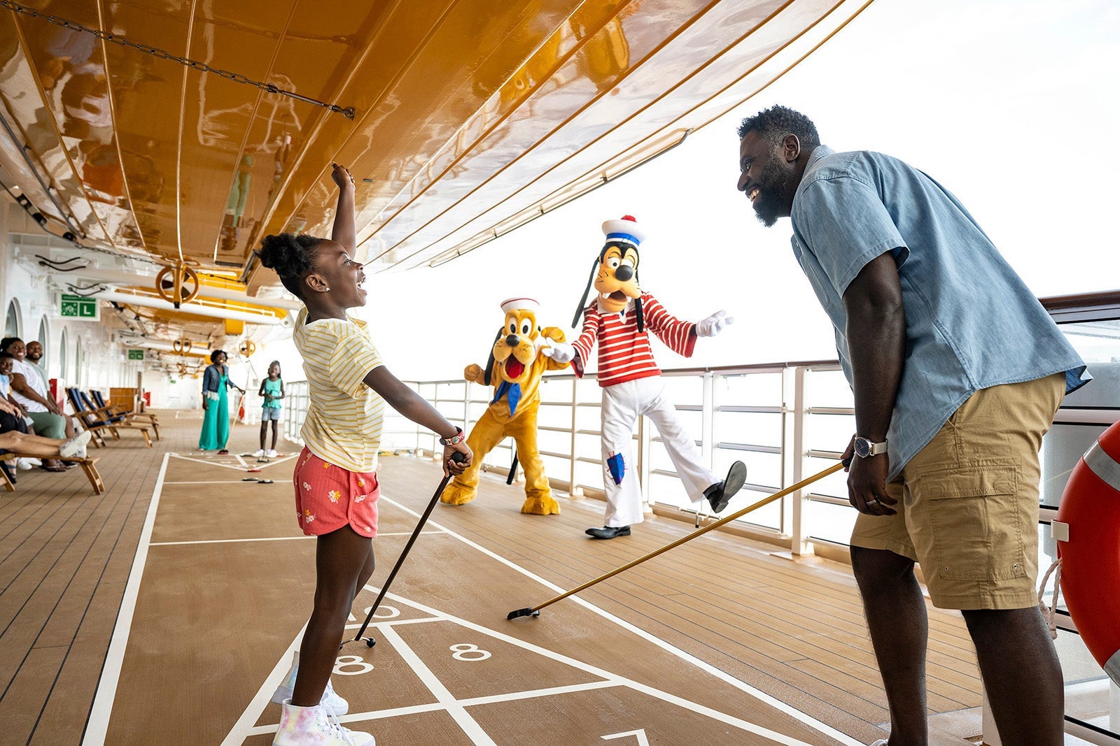 Dad and daughter playing shuffleboard on cruise ship with Goofy and Pluto watching