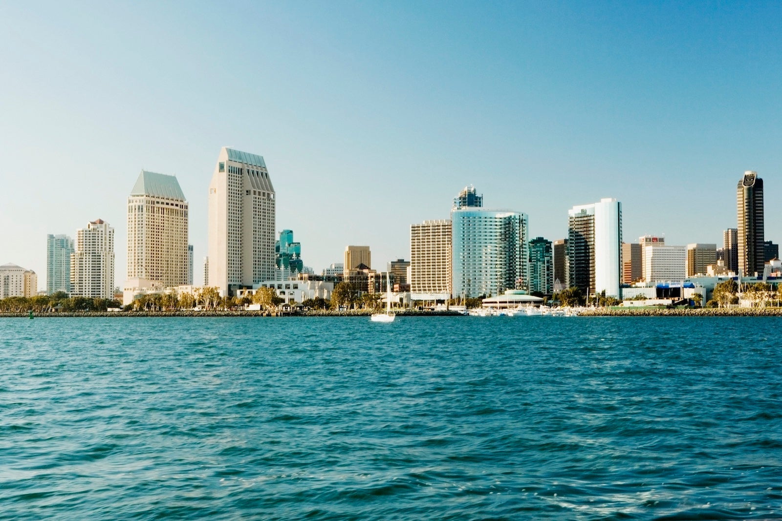 A view of the downtown San Diego skyline from the water with teal water in the foreground