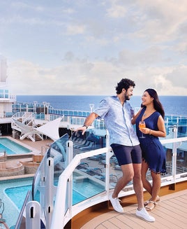 Couple standing on Sky Suite balcony overlooking pool deck and movie screen