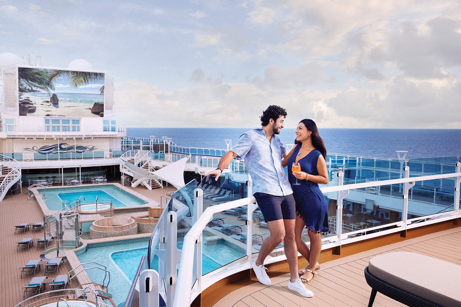 Couple standing on Sky Suite balcony overlooking pool deck and movie screen