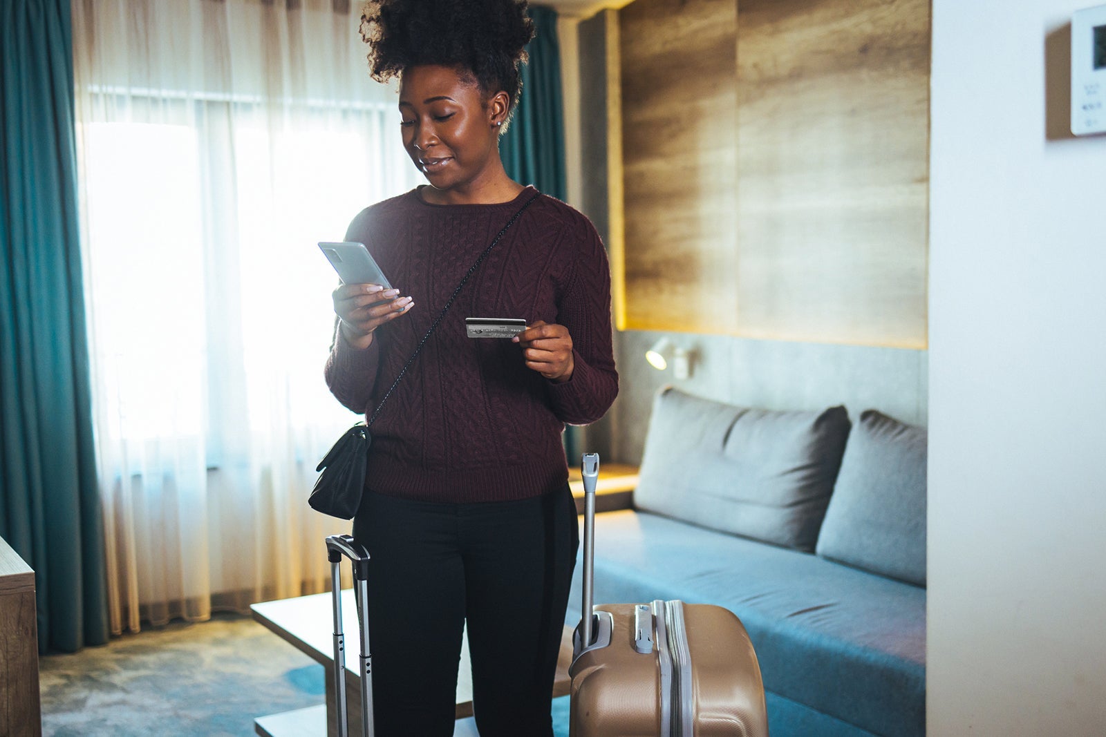 A woman holding her phone and credit card in a hotel room