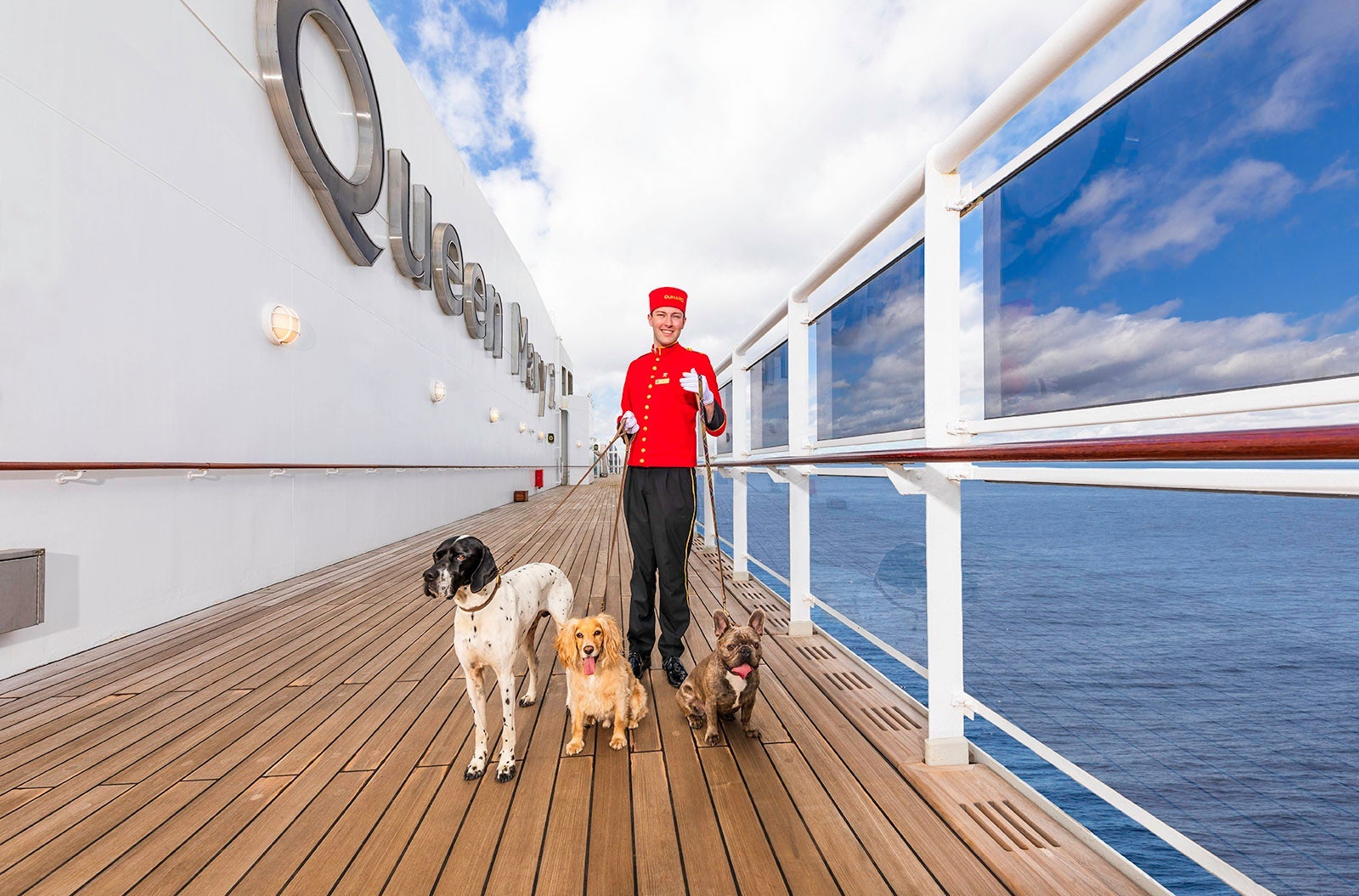 Man in red bellhop uniform walking several dogs on the deck of a cruise ship