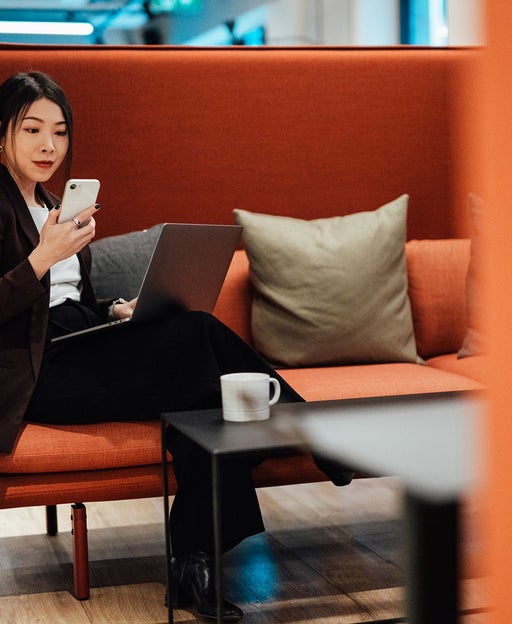 Young Asian business woman working on smartphone and laptop while sitting at airport VIP lounge with suitcase