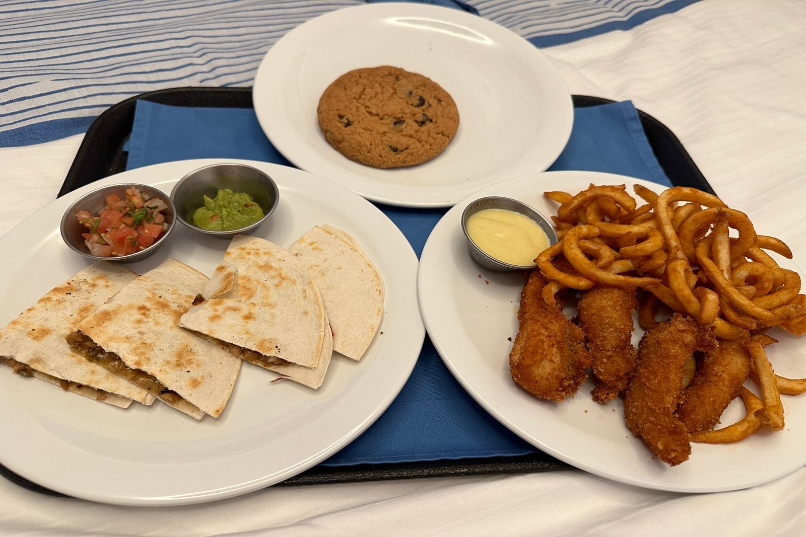 Three plates with a quesadilla, chicken fingers and fries, and cookies