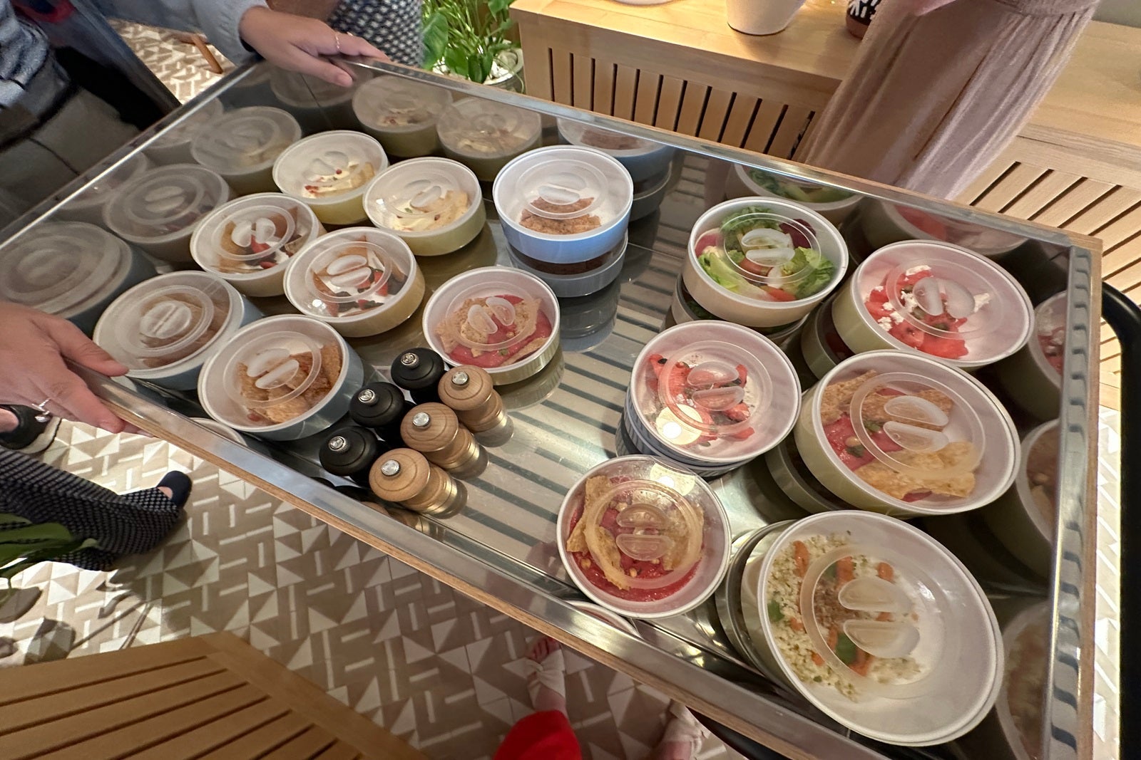 A tray of small, round bowls filled with an assortment of food and covered with plastic lids